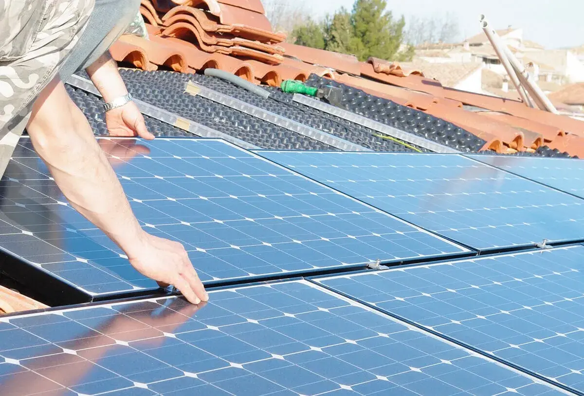 Installation de panneaux solaires sur un toit. Une main ajuste un panneau, préparant la revente du surplus photovoltaïque sans RGE.