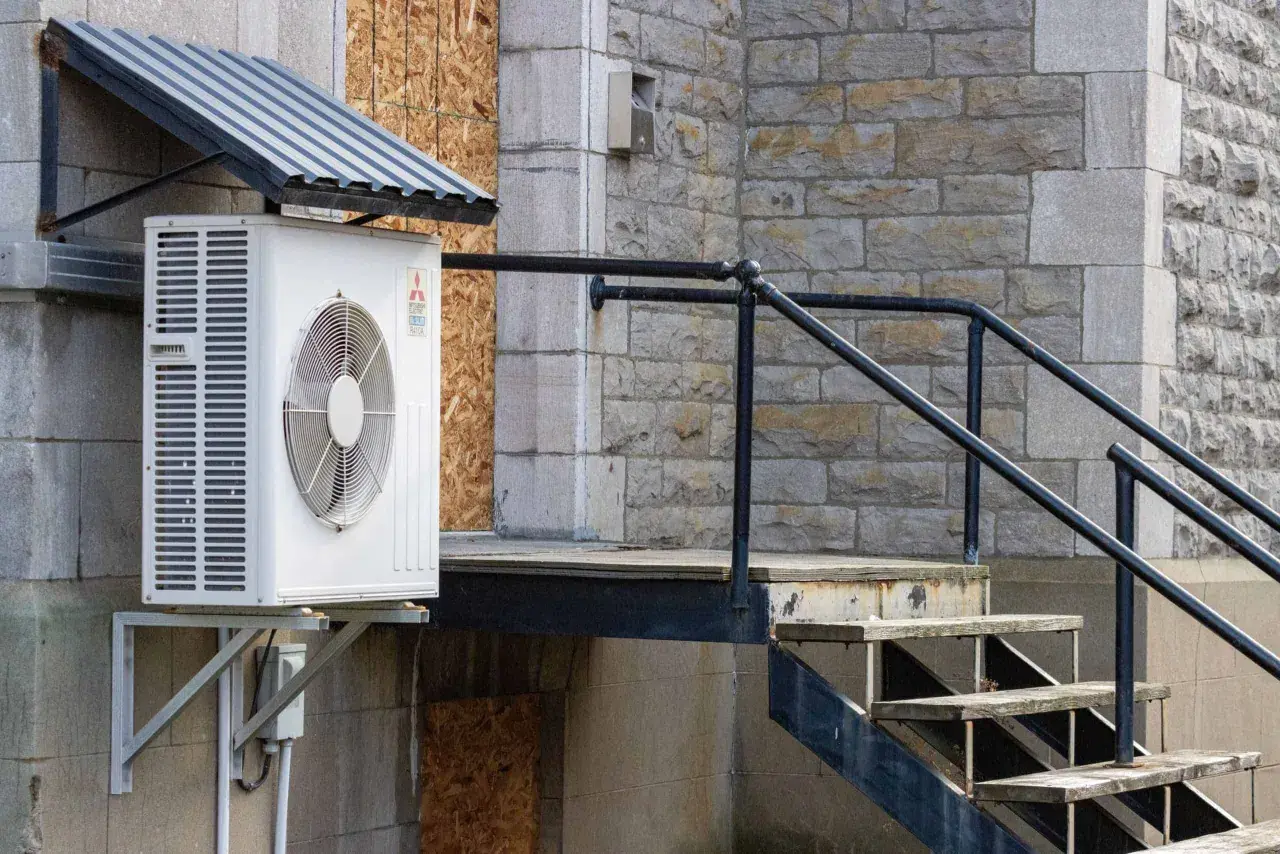 Unité extérieure de climatisation sous un auvent, près d'un escalier en métal et en bois. Idéal pour savoir où placer sonde température extérieure.