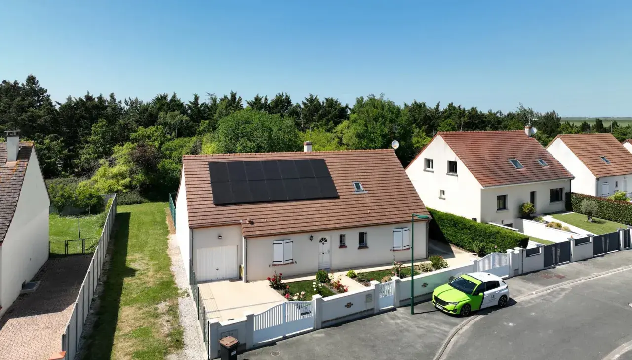 Maison avec panneaux photovoltaïques en vente, un véhicule vert et blanc garé devant.