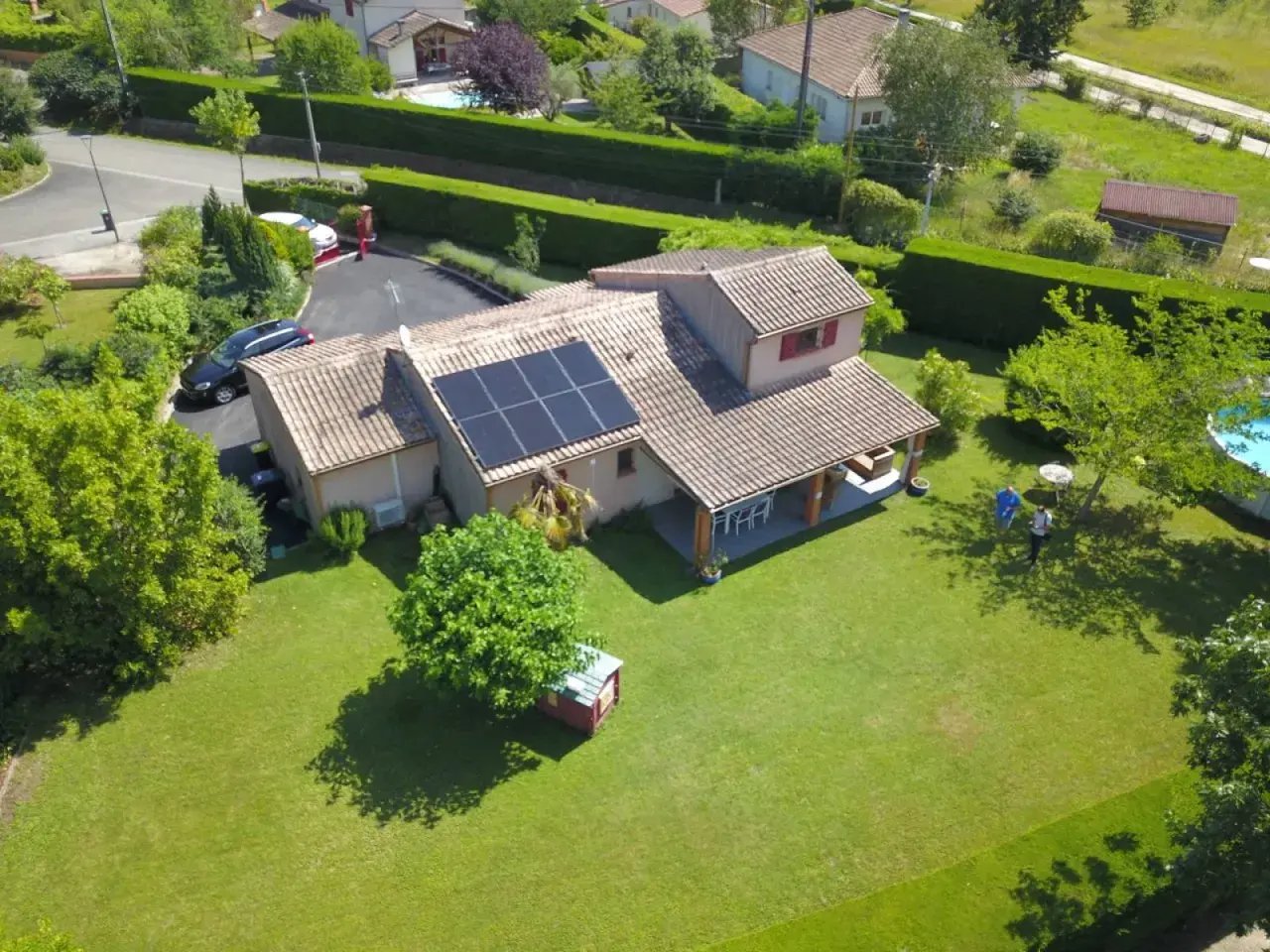 Maison avec panneaux photovoltaïques sur le toit, jardin verdoyant, piscine et deux personnes discutant.