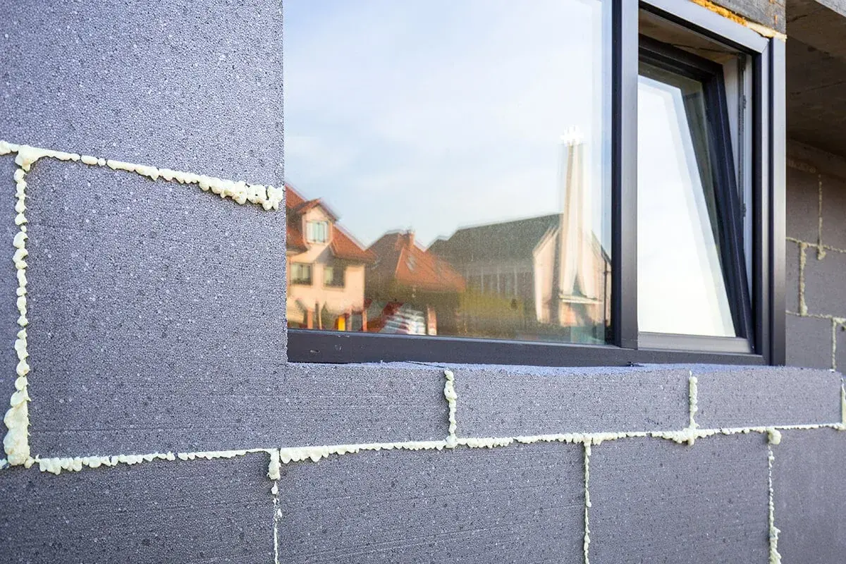Mousse isolante appliquée sur des blocs de béton pour un enduit isolant extérieur. Reflets de maisons dans la fenêtre.