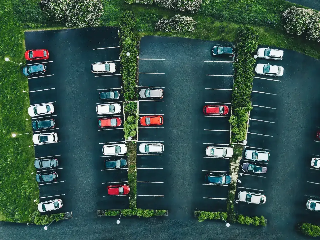 Vue aérienne d'un parking avec des voitures garées. La loi aper est respectée, avec des places bien délimitées et des espaces verts.