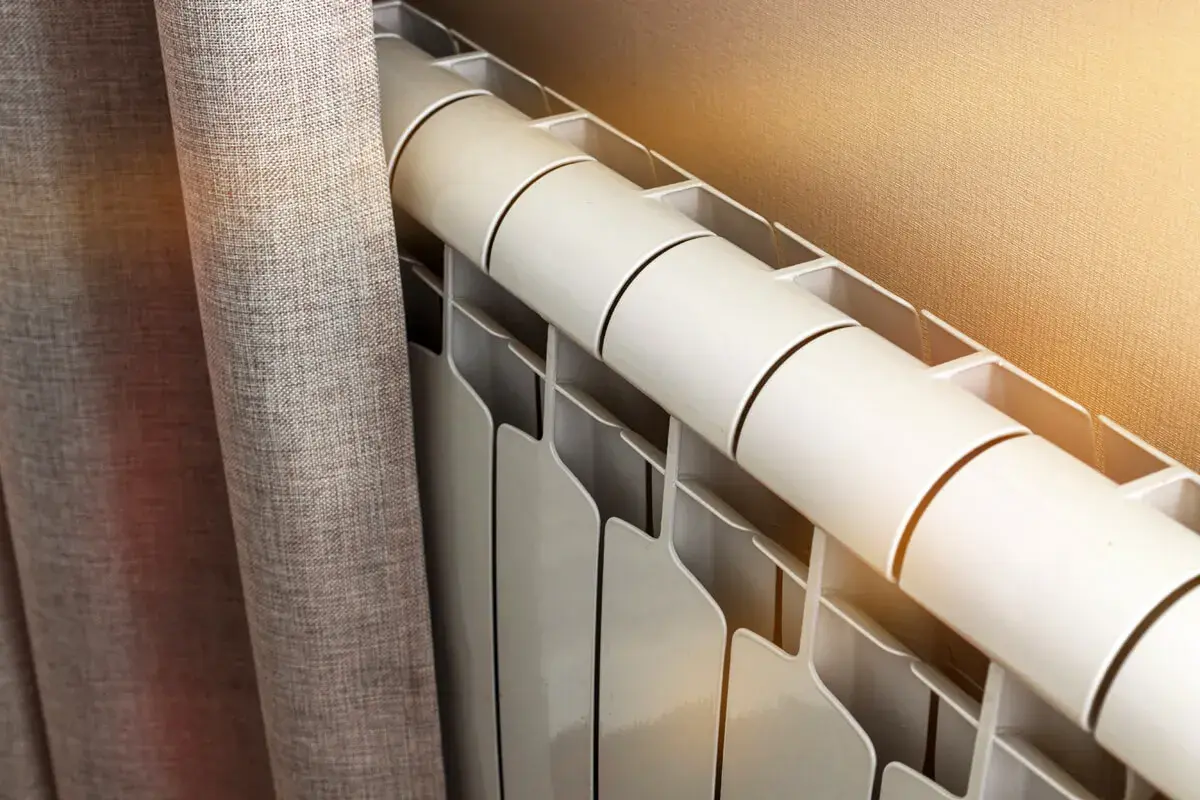 Radiateur blanc près d'un rideau gris. Le fluide caloporteur circule pour chauffer la pièce.
