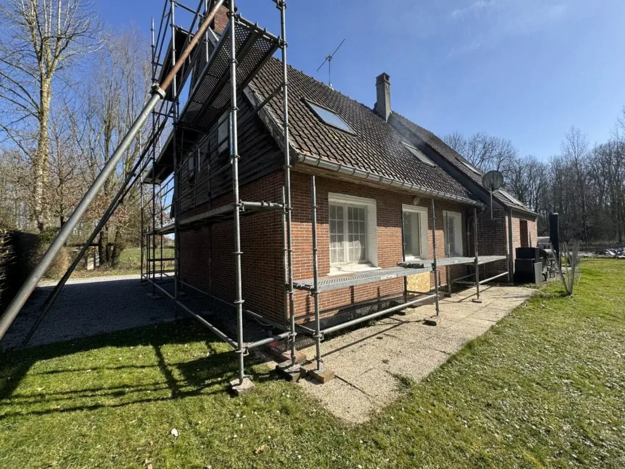 Échafaudage autour d'une maison en briques rouges, signe d'une rénovation maison de ville en cours. Le soleil brille sur le chantier.