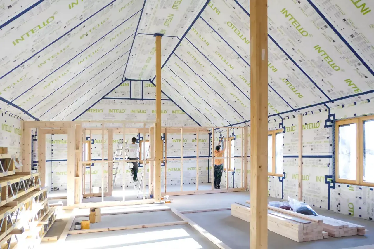 Construction d'une maison avec membrane d'étanchéité à l'air obligatoire. Des ouvriers installent la membrane sur les murs et le toit.