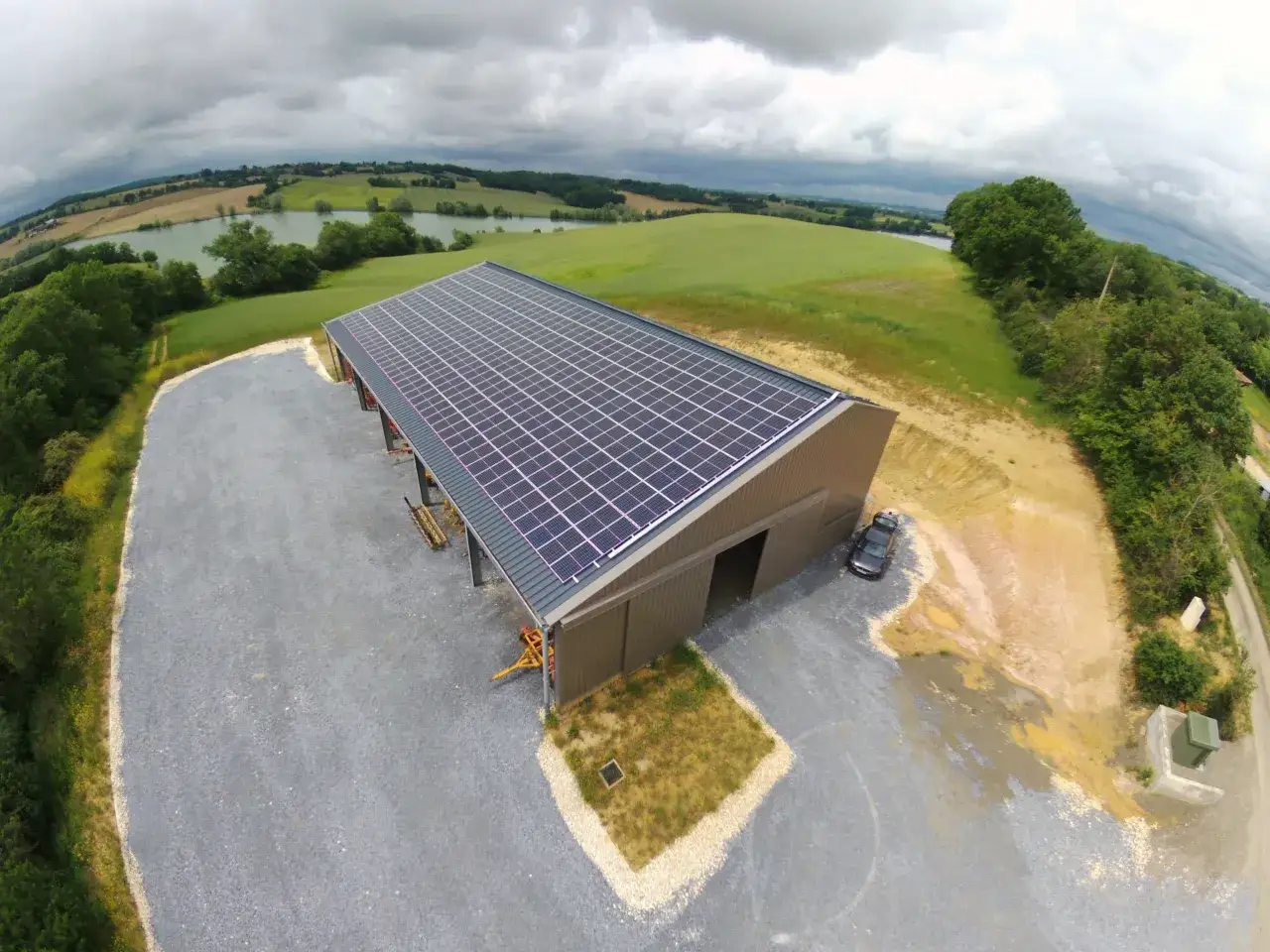 B&acirc;timent agricole avec panneaux solaires sur le toit, assurant une rentabilit&eacute; 100 kw photovolta&iuml;que. Paysage verdoyant et lac en arri&egrave;re-plan.