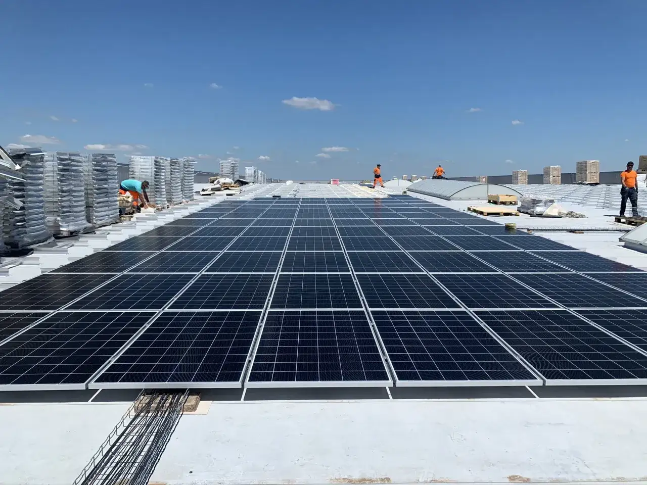Installation de panneaux photovoltaïques sur un toit. Des ouvriers travaillent sur le chantier, sous un ciel bleu. Un bureau d'étude spécialisé supervise le projet.
