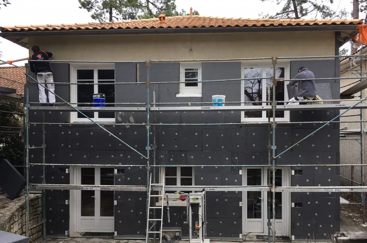 Travaux de rénovation extérieure : pose d'isolant noir sur la façade d'une maison, respectant la norme isolation thermique rénovation.