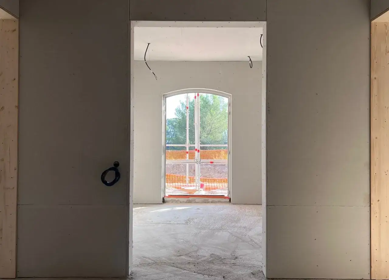 Int&eacute;rieur en cours de finition, murs en fermacell ou placo, avec une fen&ecirc;tre cintr&eacute;e donnant sur l'ext&eacute;rieur.