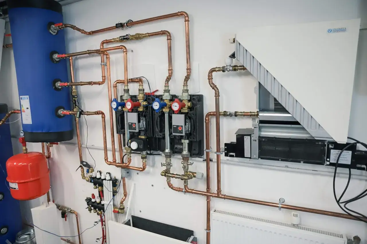 Installation d'une pompe à chaleur : réservoir bleu, tuyauterie cuivre, manomètres et unité intérieure. Idéal pour une formation.