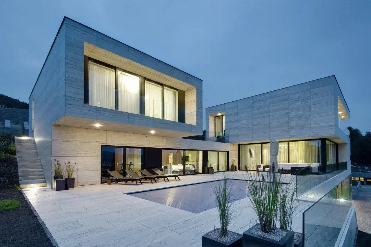 Une maison container moderne avec piscine et terrasse en pierre. L'architecture audacieuse et les grandes baies vitr&eacute;es cr&eacute;ent un espace de vie lumineux.