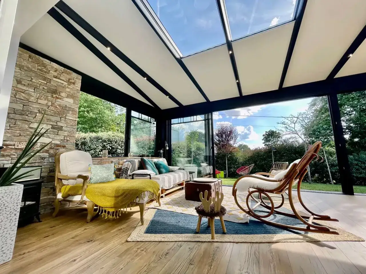 Aménagement intérieur d'une véranda avec une isolation toiture veranda par l'interieur, créant un espace cosy avec fauteuils, canapé et vue sur jardin.