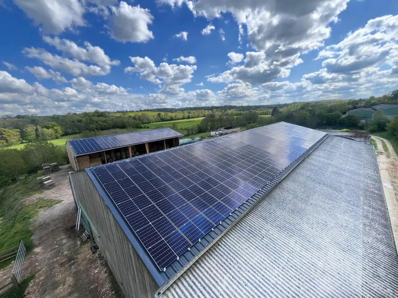 Panneaux solaires sur les toits de bâtiments agricoles, un projet photovoltaïque en Nouvelle-Aquitaine. Paysage verdoyant sous un ciel bleu nuageux.
