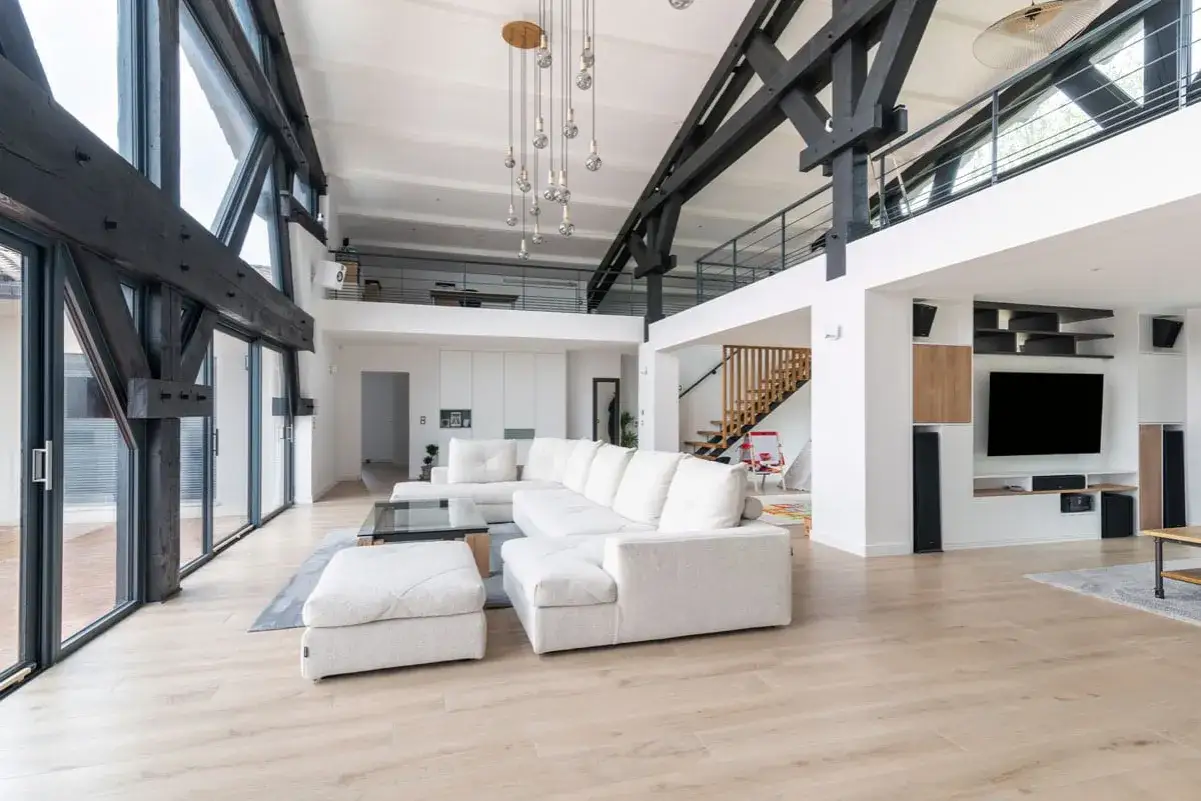 Salon moderne avec poutres apparentes, canap&eacute; blanc, escalier en bois. Le prix de r&eacute;novation de maison peut varier selon l'ampleur des travaux.