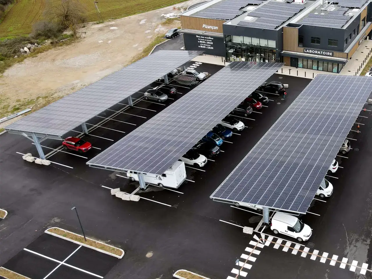 Parking ombrag&eacute; par des panneaux solaires, avec des voitures gar&eacute;es. Un panneau indique 
