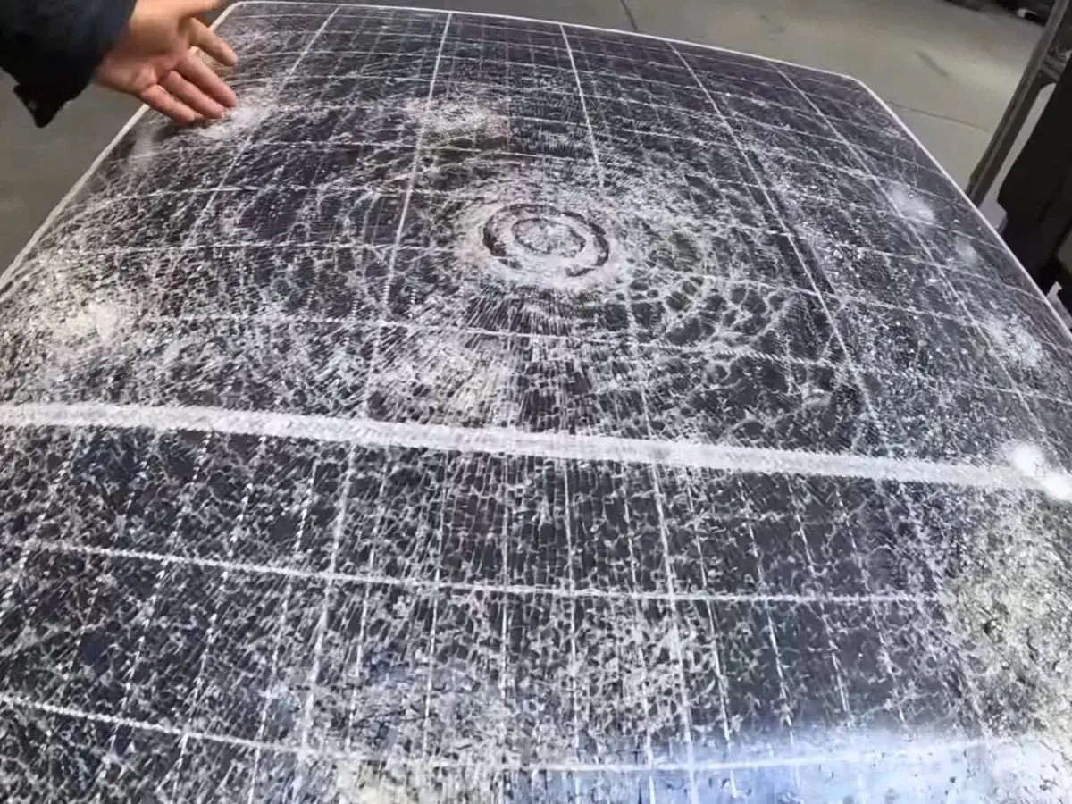 Panneau solaire endommag&eacute; par la gr&ecirc;le, montrant de multiples impacts et fissures sur sa surface.