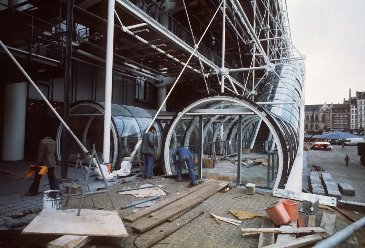 Chantier de rénovation énergétique des bâtiments publics : ouvriers travaillant sur une structure extérieure vitrée et métallique.
