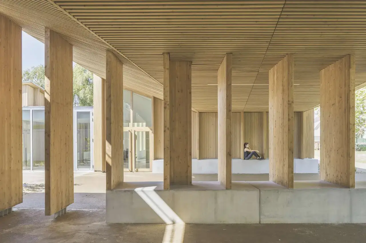 Une personne assise sous une impressionnante structure bois, avec des piliers massifs et un plafond lamellé.