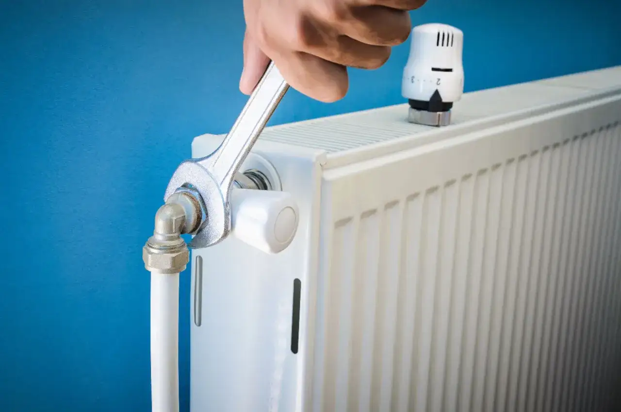 Main tenant répare un radiateur qui fait du bruit avec une clé.