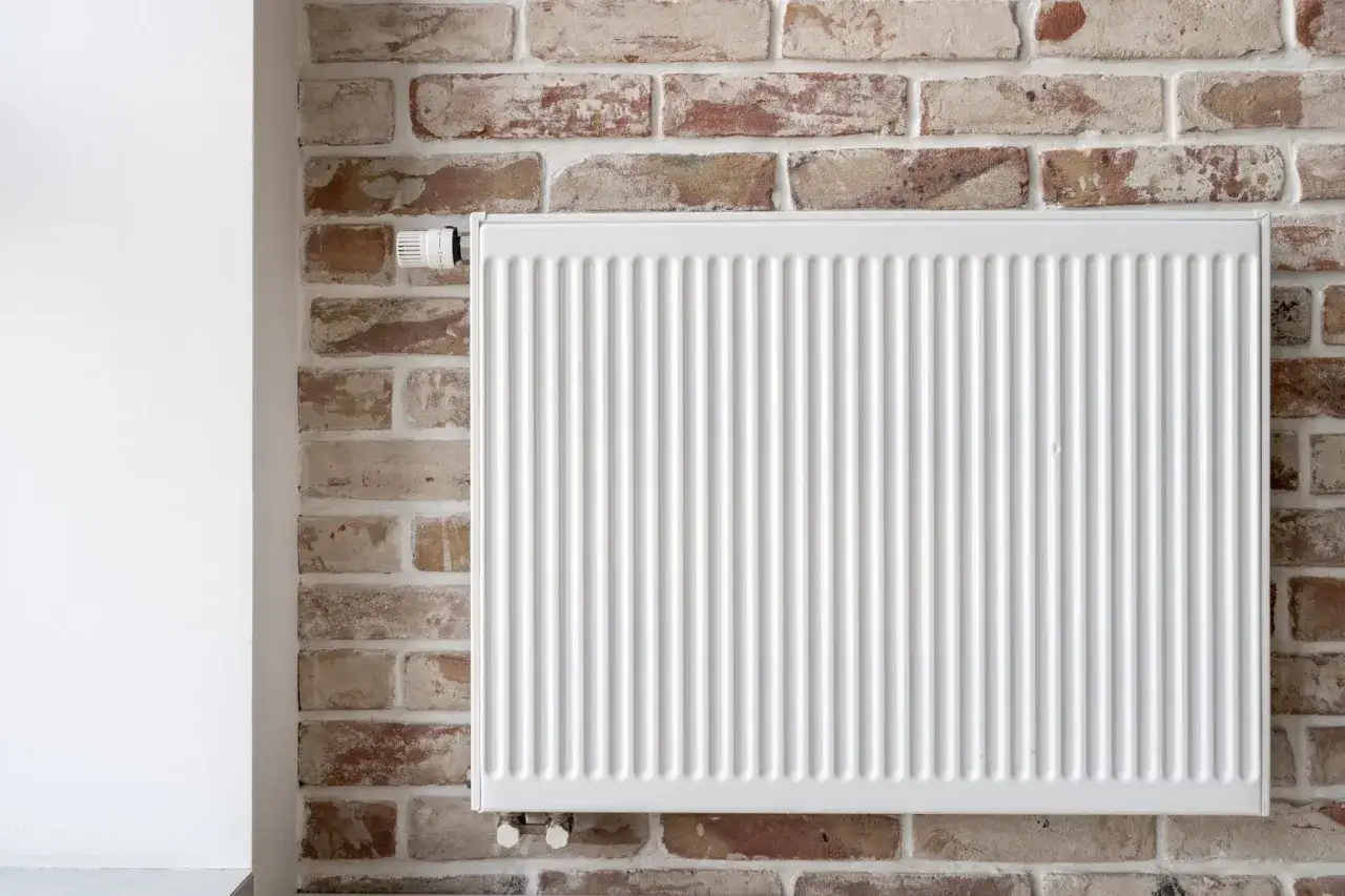 Un radiateur blanc est fix&eacute; sur un mur de briques apparentes. Le thermostat est visible sur le c&ocirc;t&eacute; gauche. Ce mur chauffant assure une ambiance chaleureuse.