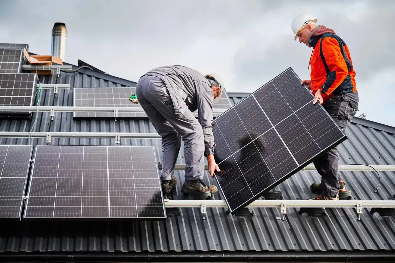 Deux techniciens installent des panneaux solaires sur un toit. Ce bâtiment photovoltaïque produira bientôt de l'énergie verte.