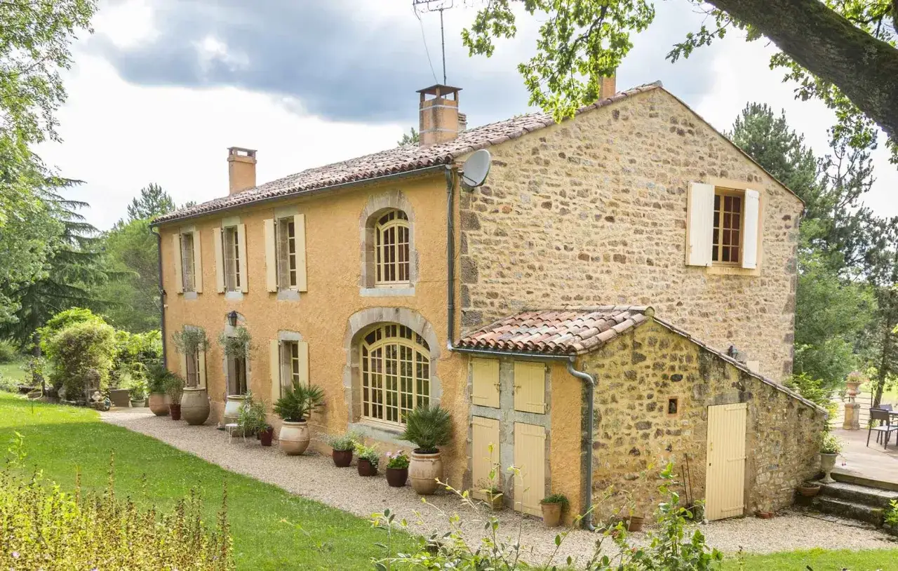 Belle ferme rénovée avec murs en pierre et enduit ocre, entourée d'un jardin verdoyant.