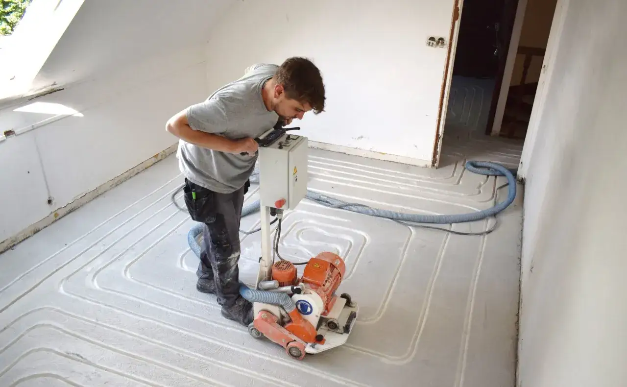 Un ouvrier utilise une machine pour aplanir la chape d'un plancher rafra&icirc;chissant.