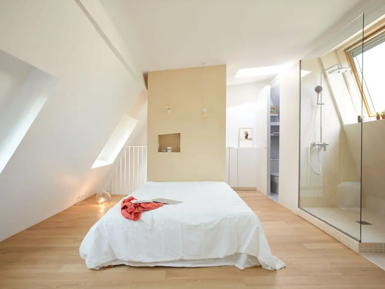 Chambre lumineuse sous les toits, résultat d'une rénovation combles réussie. Lit blanc, douche vitrée, ambiance zen.
