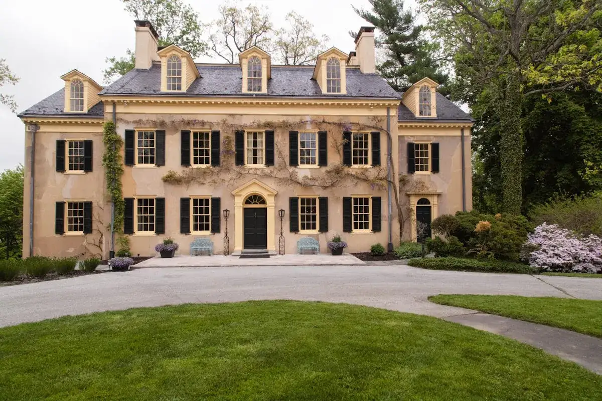 La rénovation maison de maître a redonné vie à cette demeure historique aux volets noirs et aux fenêtres claires, entourée d'un jardin verdoyant.