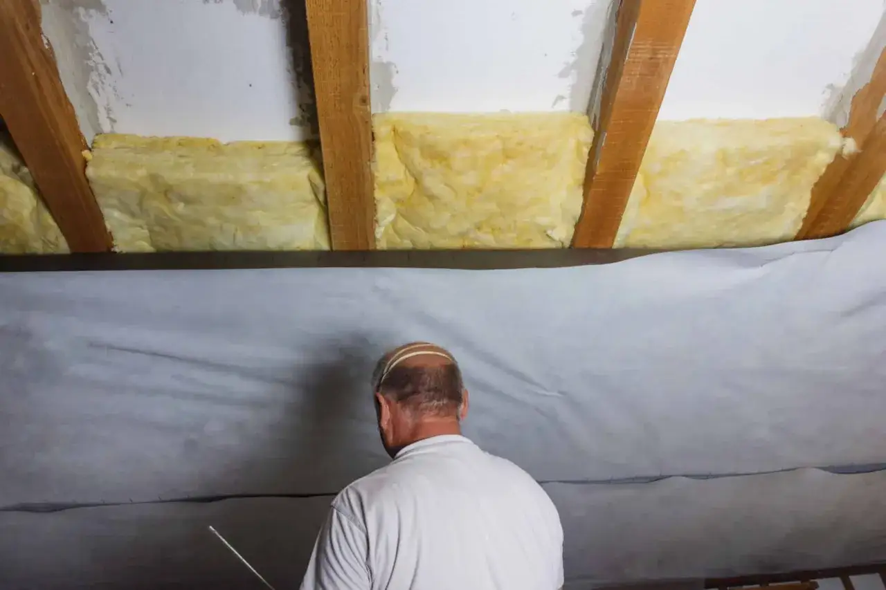 Un homme installe une isolation laine de verre sous les combles, une étape essentielle pour le confort thermique.