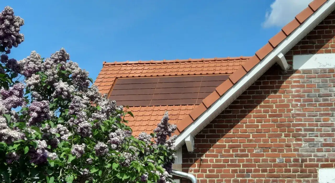 Panneaux solaires discrets sur un toit de tuiles, entourés de lilas en fleurs, dans une zone classée.