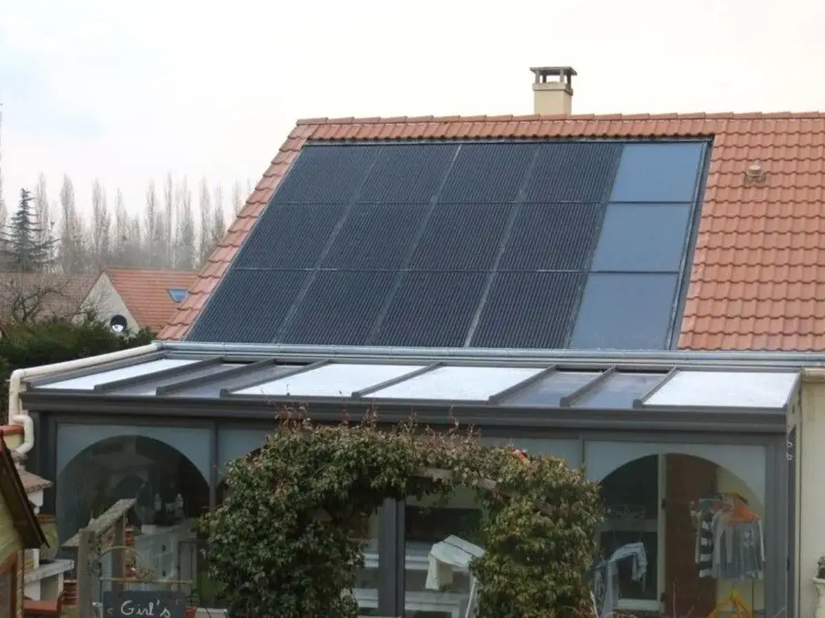 Panneaux solaires aérovoltaïques intégrés sur un toit de tuiles rouges, au-dessus d'une véranda vitrée.