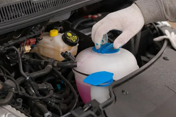 Main d'une personne portant un gant blanc ferme le bouchon d'un vase d'expansion rempli d'eau et de liquide de refroidissement rose.
